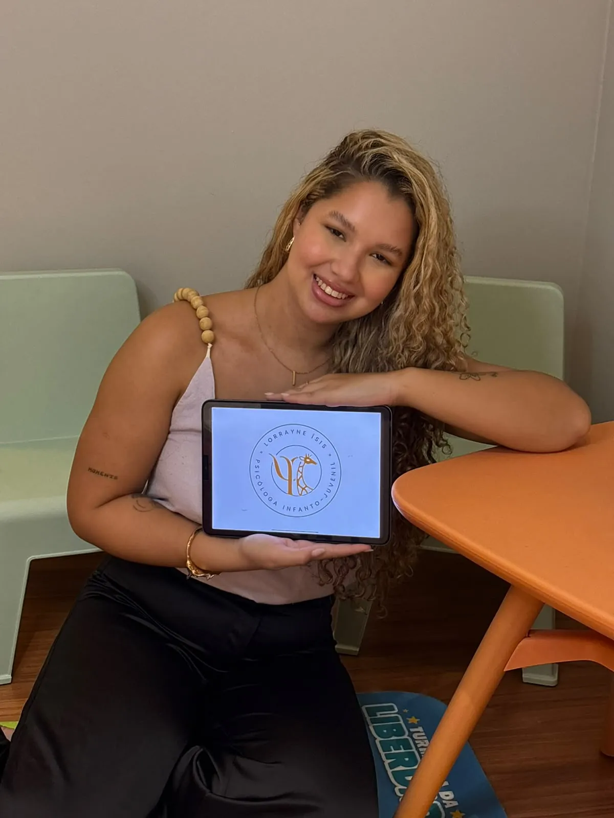 Lorrayne Ísis, psicóloga, sorrindo no consultório com a logo dela no tablet
