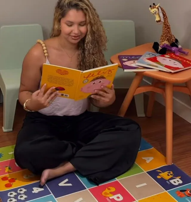 Lorrayne Ísis lendo um livro infantil no tapete do consultório